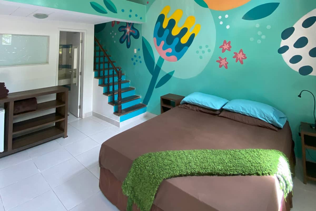 Ein Schlafzimmer mit Bett, Treppe, einer Wand mit abstrakter Kunst und einem Deckenventilator.