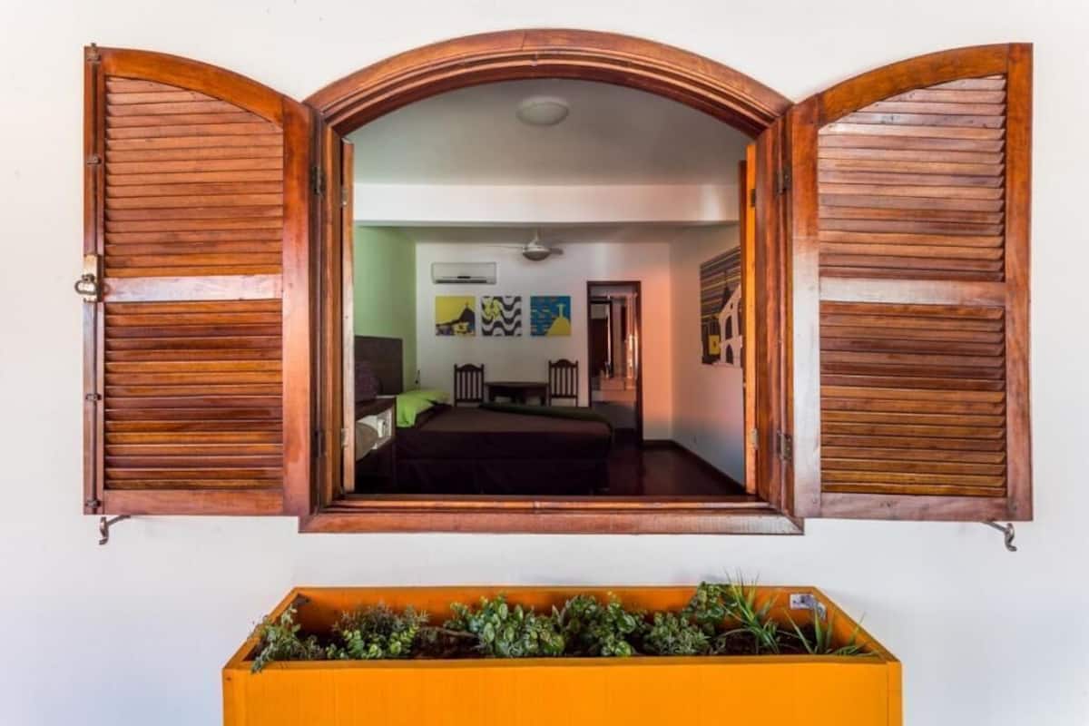 Ein Zimmer mit Bett, Schreibtisch und Stuhl, einem Fenster mit Holzjalousien sowie einer Wand-Klimaanlage.