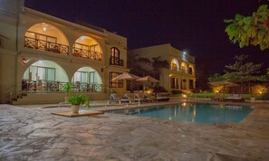A large building with multiple balconies, a swimming pool, and outdoor seating. - Mzima Beach Resort (Diani Beach)