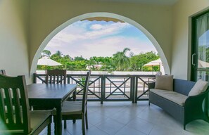 A covered outdoor seating area with a table and chairs, a sofa, and a view of greenery and buildings. - Mzima Beach Resort (Diani Beach)