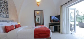 A hotel room with a bed, a television, a mirror, and a sliding glass door to a balcony. - Mzima Beach Resort (Diani Beach)