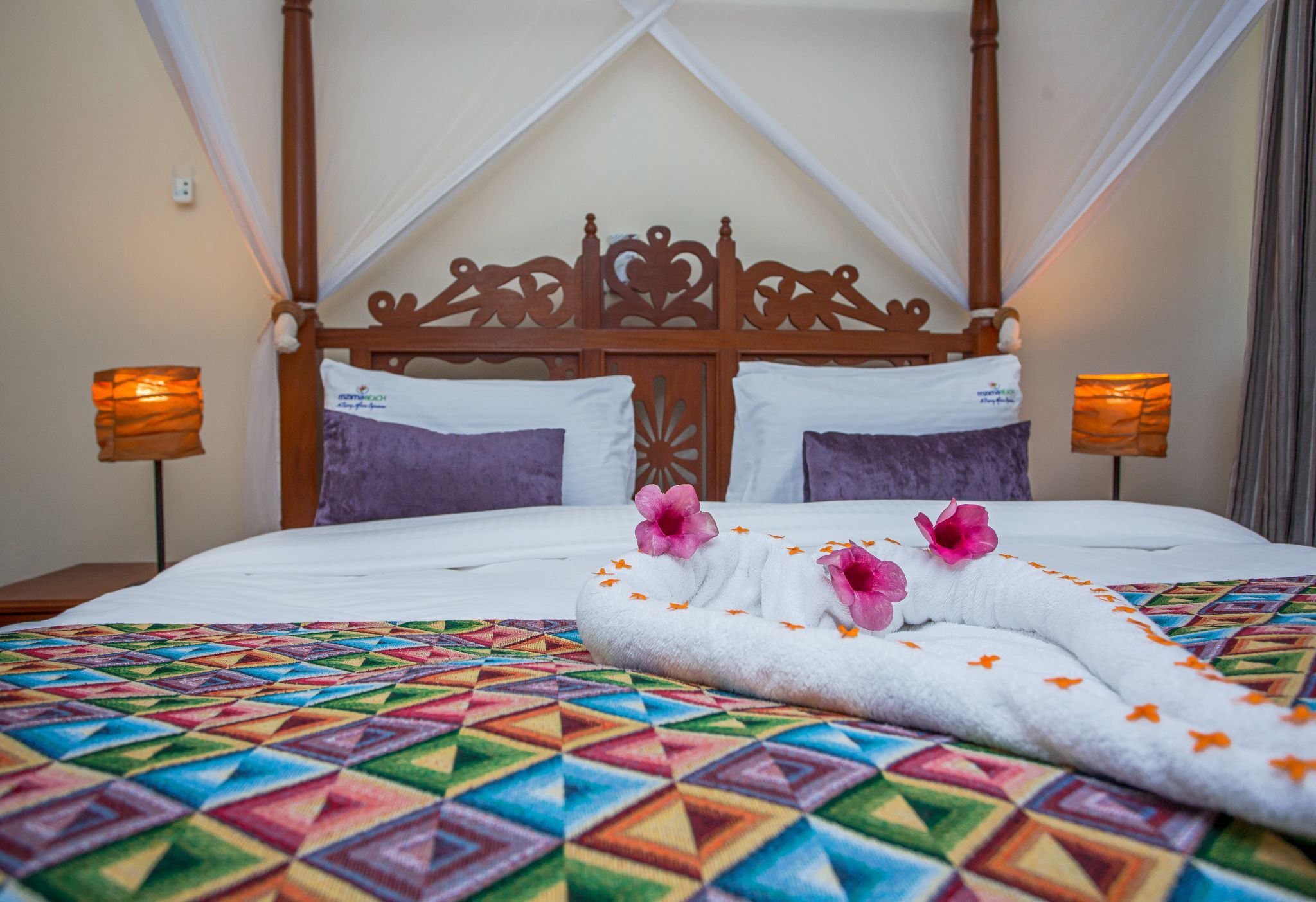 A bed with a geometric patterned bedspread, a wooden headboard, and two bedside lamps.