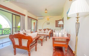 A spacious room with a wooden sofa, a dining table, and a lamp. - Mzima Beach Resort (Diani Beach)