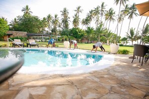 A swimming pool with lounge chairs and a stone deck, surrounded by palm trees. - Mzima Beach Resort (Diani Beach)