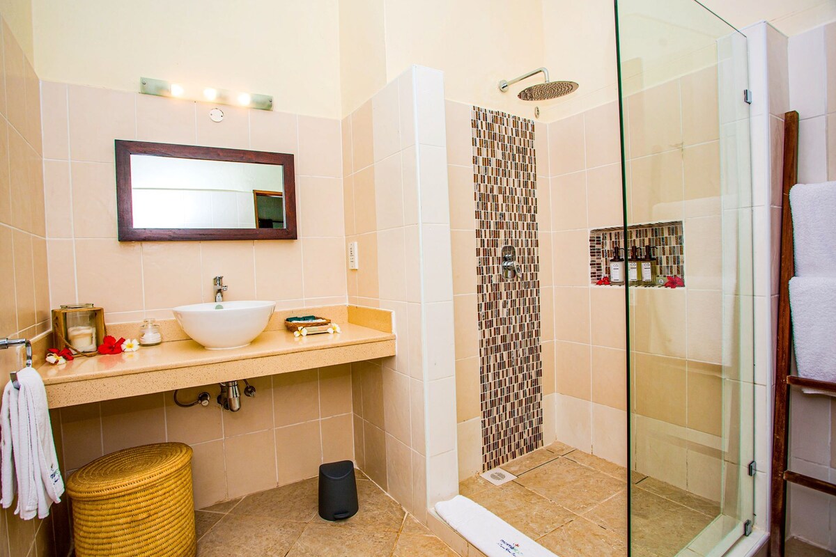 A bathroom with a sink, mirror, shower, and glass-enclosed shower stall.