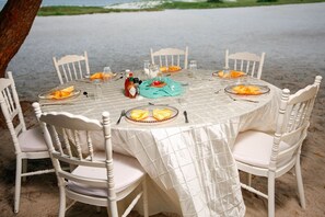 A round table set for six with white chairs, a tablecloth, and plates of food. - Mzima Beach Resort (Diani Beach)