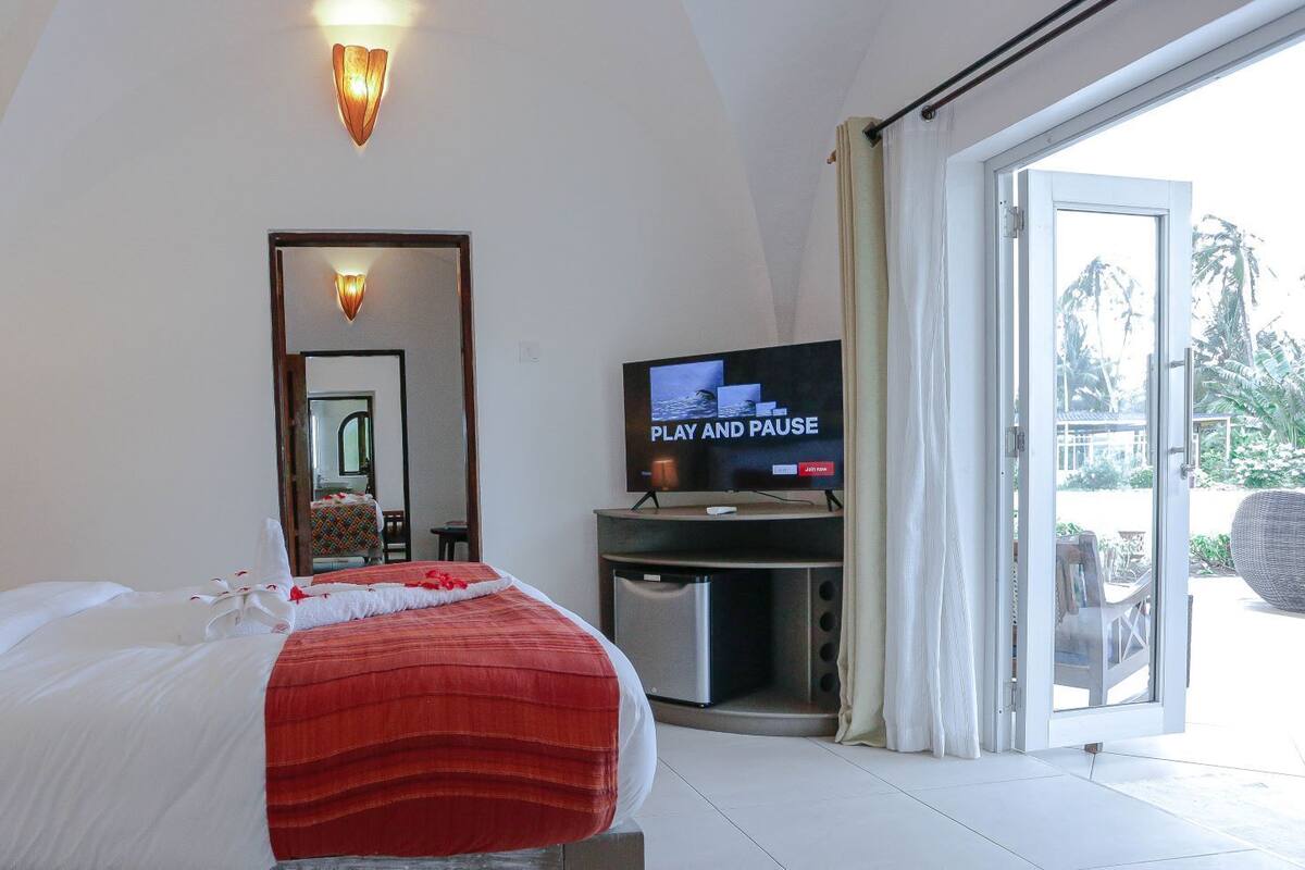 A hotel room with a bed, a television, a mirror, and a sliding glass door to a balcony.