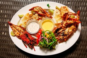A plate of grilled seafood with lemon wedges and a side salad. - Mzima Beach Resort (Diani Beach)