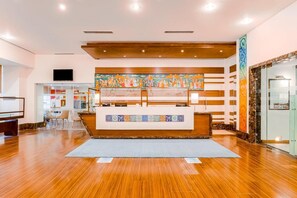 A reception area with a wooden reception desk, a colorful mural, and a modern interior design. - Club Mahindra Jaipur (Jalsu)