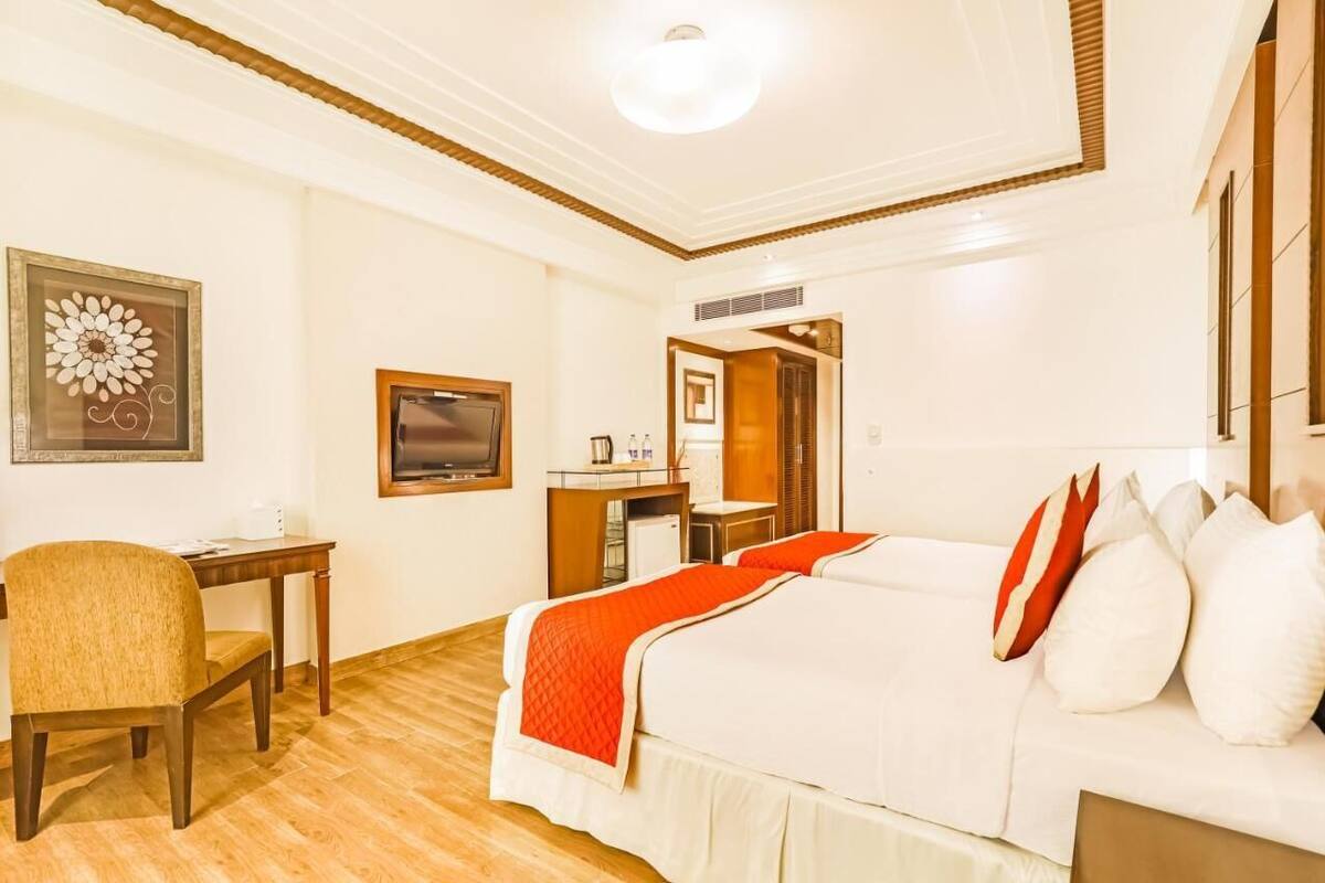 Una habitación de hotel con una cama, un escritorio, una silla, un televisor y una obra de arte enmarcada en la pared.