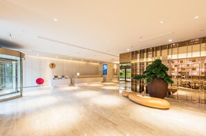Eine moderne Hotellobby mit Empfangstresen, einer großen Pflanze und einer Sitzecke mit Glaswand.