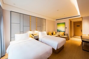 Ein Hotelzimmer mit zwei Betten, einer Sitzecke mit Tisch und Stühlen sowie einem Bild an der Wand.