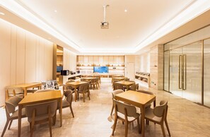 A modern hotel dining area with wooden tables and chairs, a kitchen in the background, and a glass-fronted refrigerator. - JI Hotel Chongqin Liangjiang Xingfu Plaza (Chongqing)