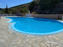 Una piscina con cubierta de piedra, rodeada por una valla y árboles.