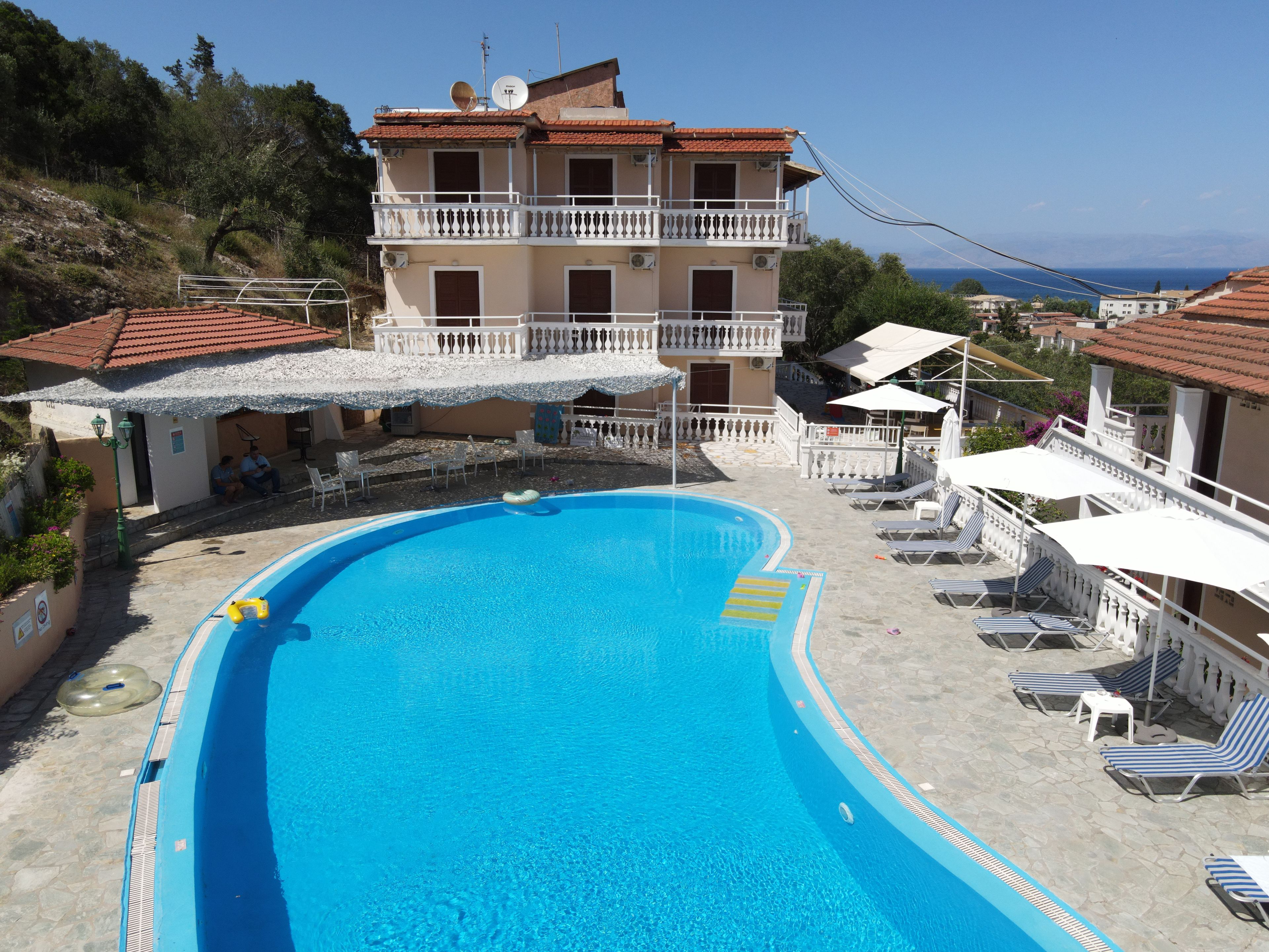 Una piscina con sillones de descanso y sombrillas, rodeada de edificios con balcones y vistas al mar.