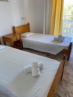 A hotel room with two single beds, a wooden nightstand, and a window with curtains.