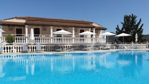 A swimming pool with lounge chairs and umbrellas, a building with a tiled roof, and a white fence. - Corfu Panorama (Corfu)