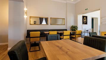 A hotel room with a wooden dining table, yellow chairs, a black sofa, and a mirror on the wall.
