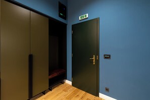 Ein Zimmer mit blauer Wand, Holzboden, einer schwarzen Tür mit goldener Griff und einer Bank.