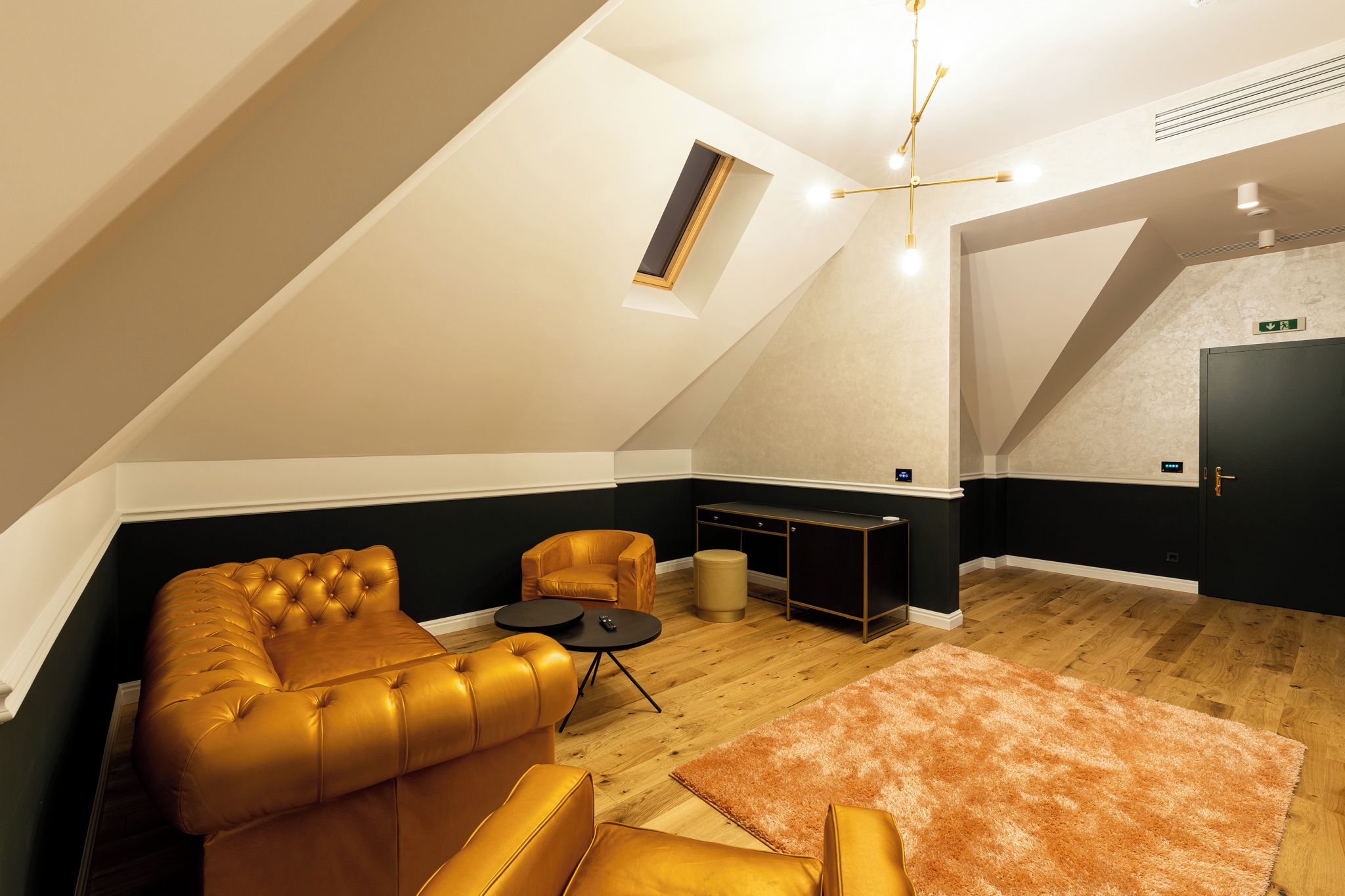 A modern loft bedroom with a sloped ceiling, a sofa, a chair, a small table, and a rug.