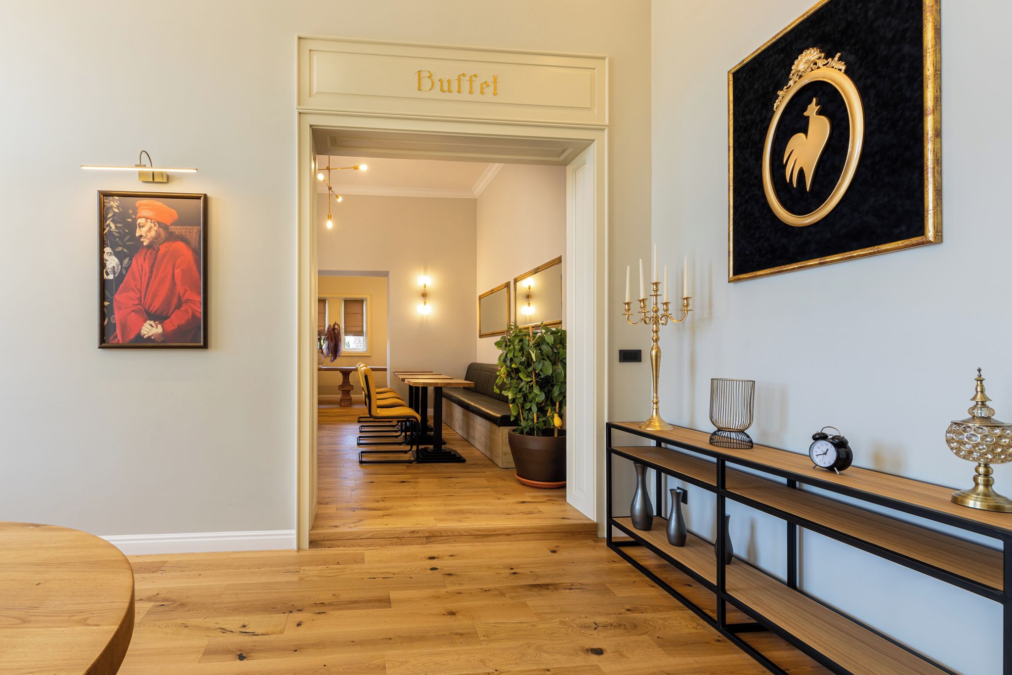 A hallway with a 'Buffet' sign, a framed artwork, a potted plant, a console table with a candelabra, and a clock.