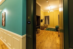 A room with a wooden floor, a green sofa, a television, and a door leading to another room. - Boutique Hotel Cocosul De Aur (Târgu Mureș)