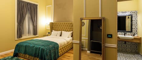 A hotel room with a bed, a bedside table, a mirror, and a bathroom with a sink and toilet.