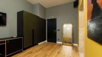 A room with a wooden floor, a black and gold cabinet, a door with an emergency exit sign, and a large mirror with a gold frame.
