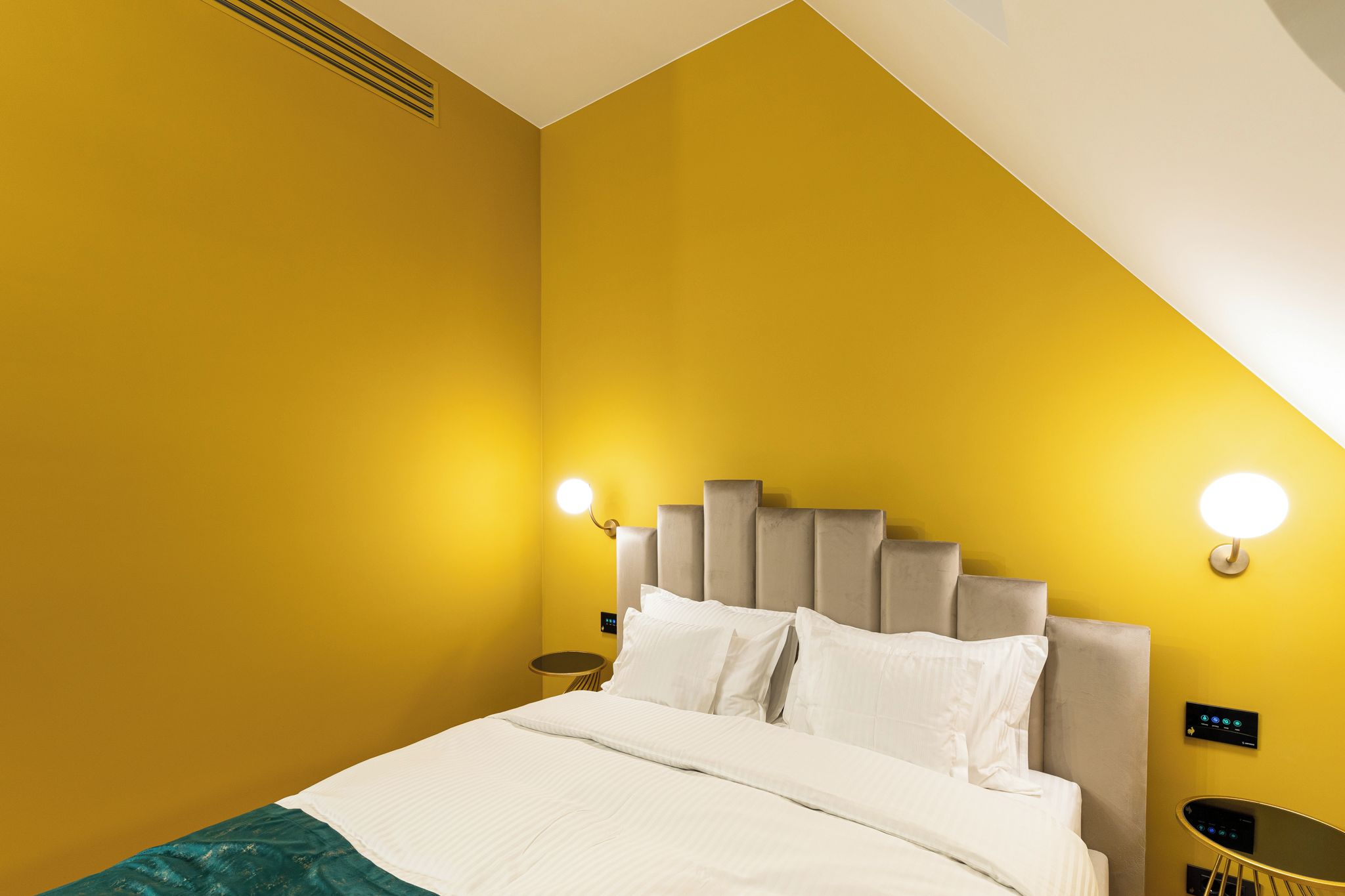 A hotel room with a bed, a headboard, bedside tables, and wall-mounted lighting.