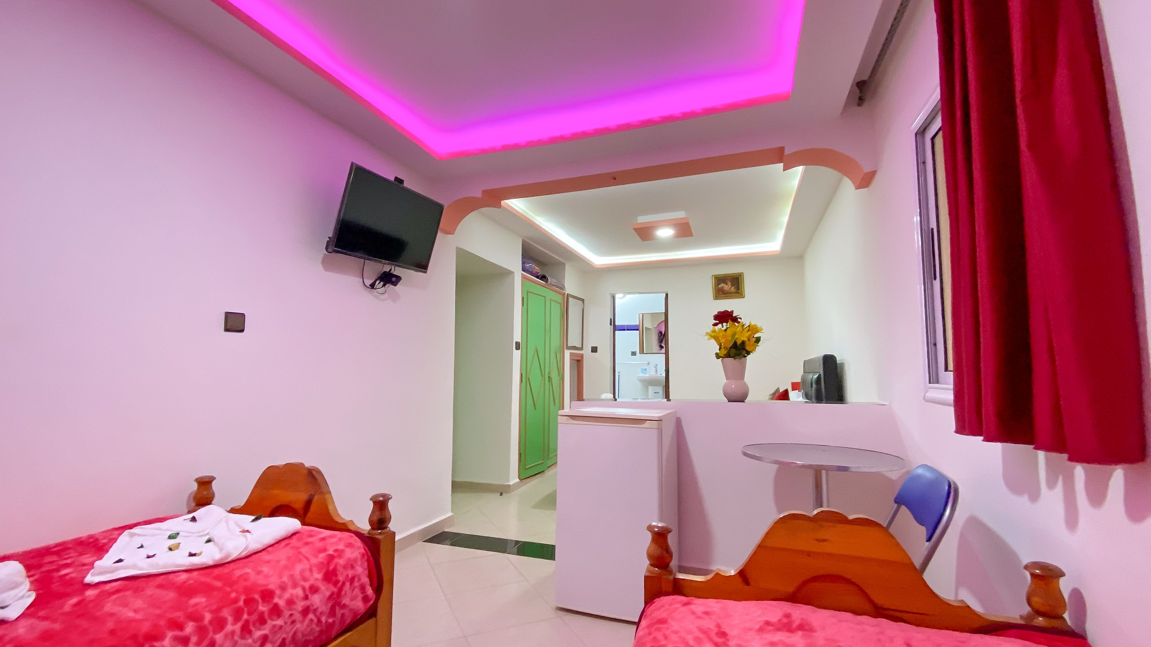 Una habitación con dos camas, un televisor montado en la pared, un escritorio con espejo y un baño visible a través de una puerta abierta.