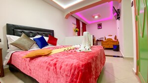 Una habitación de hotel con cama, almohadas, mesita de noche, cómoda y espejo.