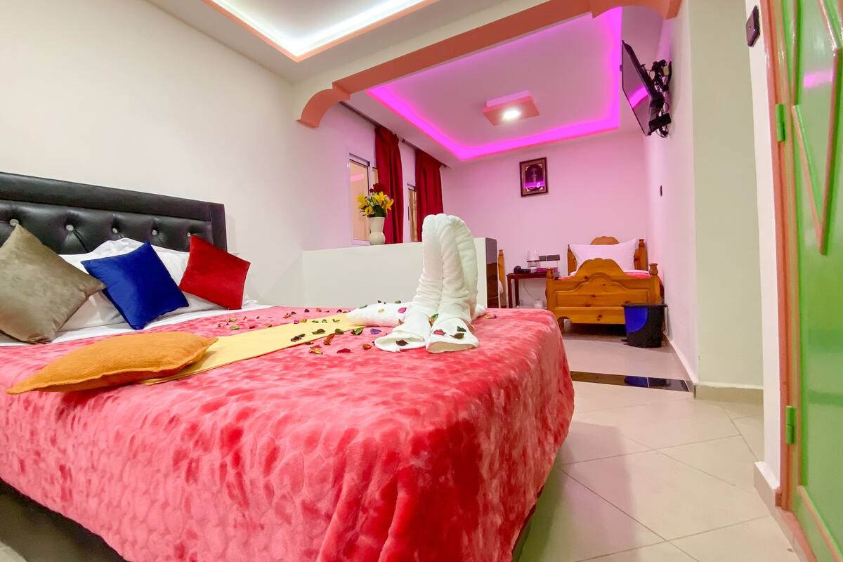 Una habitación de hotel con cama, almohadas, mesita de noche, cómoda y espejo.