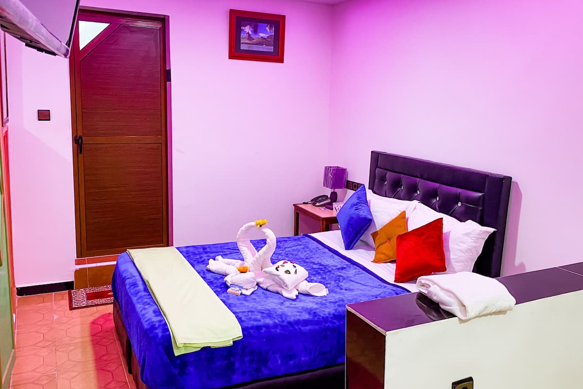 Una habitación de hotel con cama, mesita de noche, lámpara y puerta.