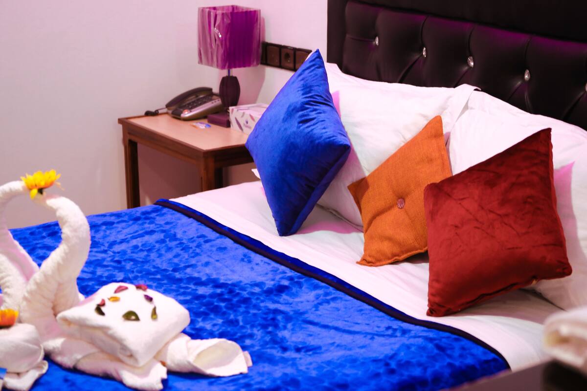 Habitación de hotel con cama, almohadas, mesita de noche con lámpara y teléfono.