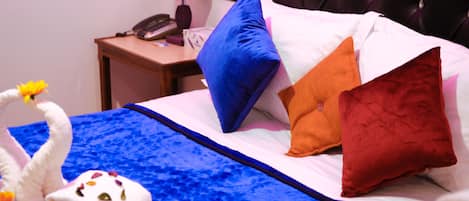 A hotel room with a bed, pillows, a nightstand with a lamp, and a telephone.