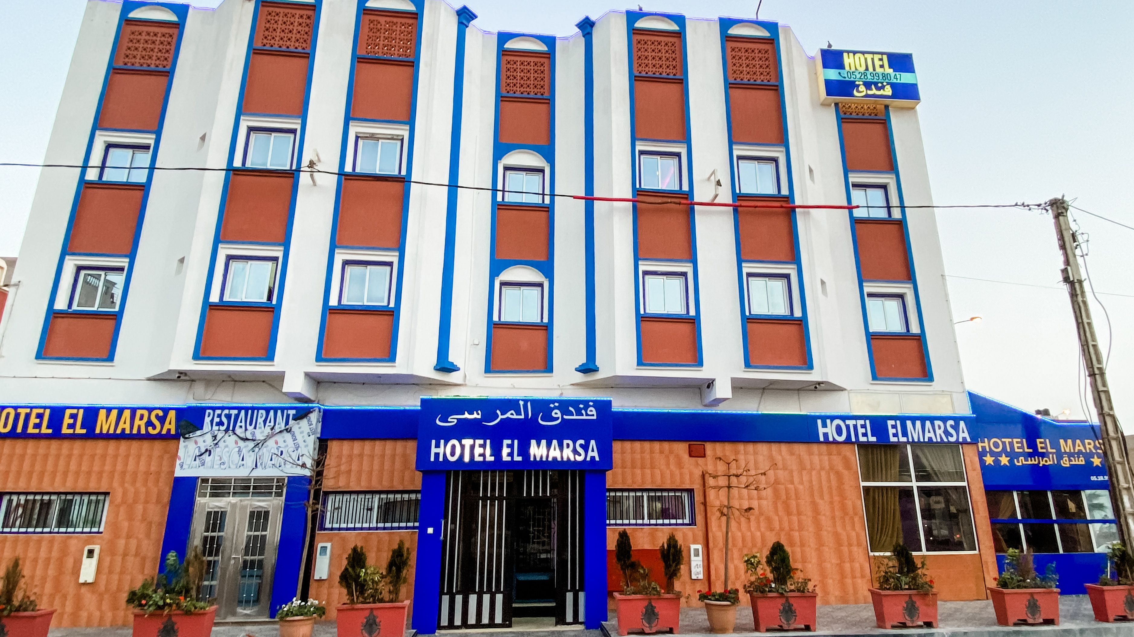 A hotel with a blue and orange facade, multiple windows, and a sign indicating it is a hotel.