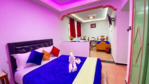 Una habitación de hotel con cama, mesita de noche, escritorio, silla y ventana con cortinas.