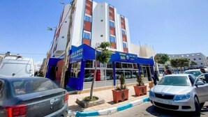 A multi-story hotel with a blue and white facade, a visible entrance, and several potted plants in front.