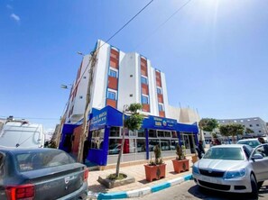 Ein mehrstöckiges Hotel mit blau-weißer Fassade, einem gut sichtbaren Eingang und mehreren Blumentöpfen davor.
