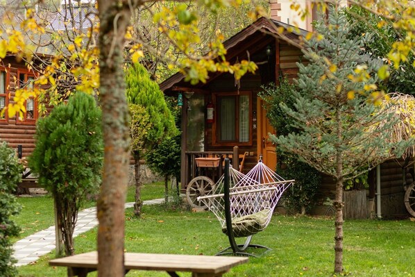 A log cabin with a garden, a swing chair, and a wooden bench.