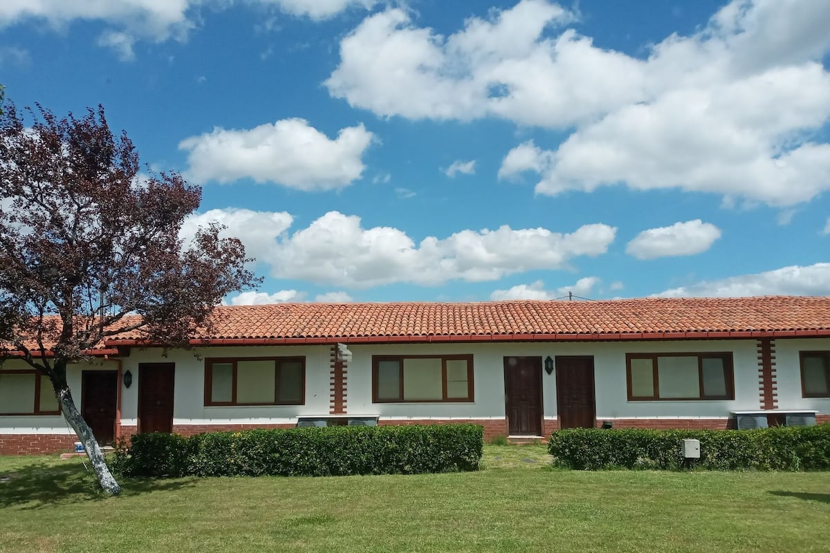 A row of motel rooms with a red-tiled roof, a grassy lawn, and a tree to the left.