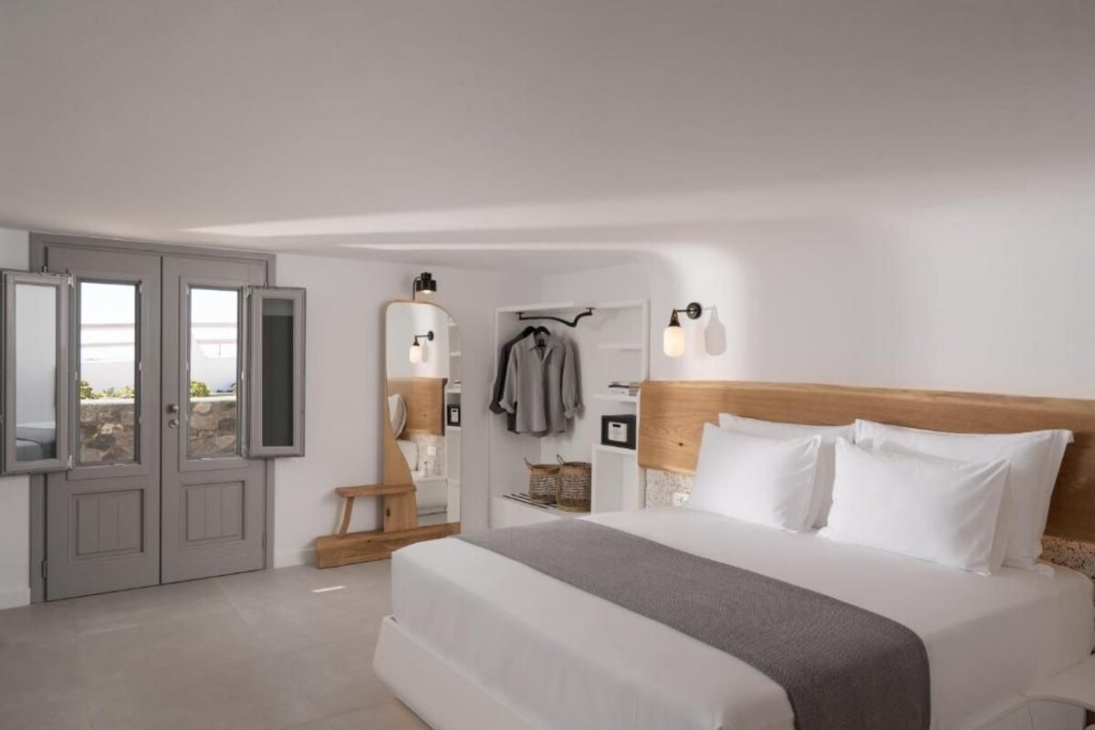 A bedroom with a bed, a wardrobe, a mirror, a bench, and a wall-mounted light fixture.