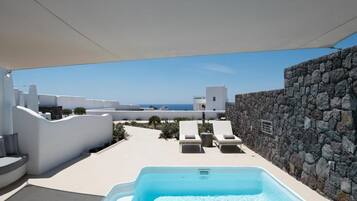 A rooftop pool area with a clear view of the sea, white buildings, and a stone wall.