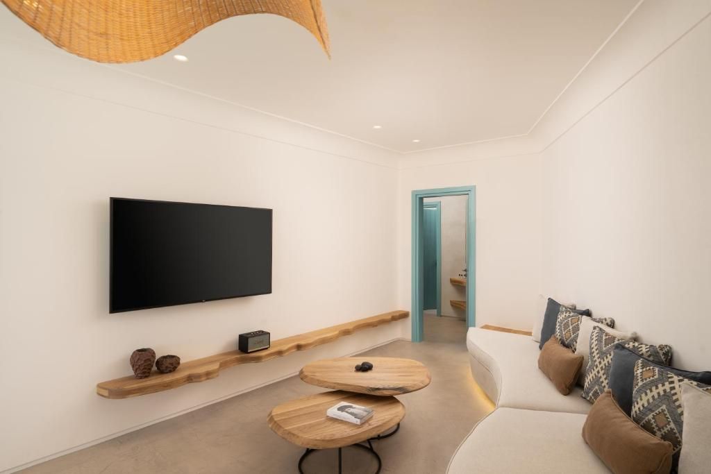 Una sala de estar moderna con un televisor de pantalla plana montado en la pared, una mesa de centro de madera y un sofá con cojines estampados.