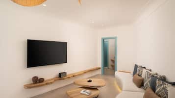 Una sala de estar moderna con un televisor de pantalla plana montado en la pared, una mesa de centro de madera y un sofá con cojines estampados.