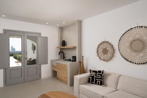 A modern living room with a sofa, a coffee table, a kitchen area with a sink and counter, and decorative wall art. - La Ponta Villas&suites (Santorini)