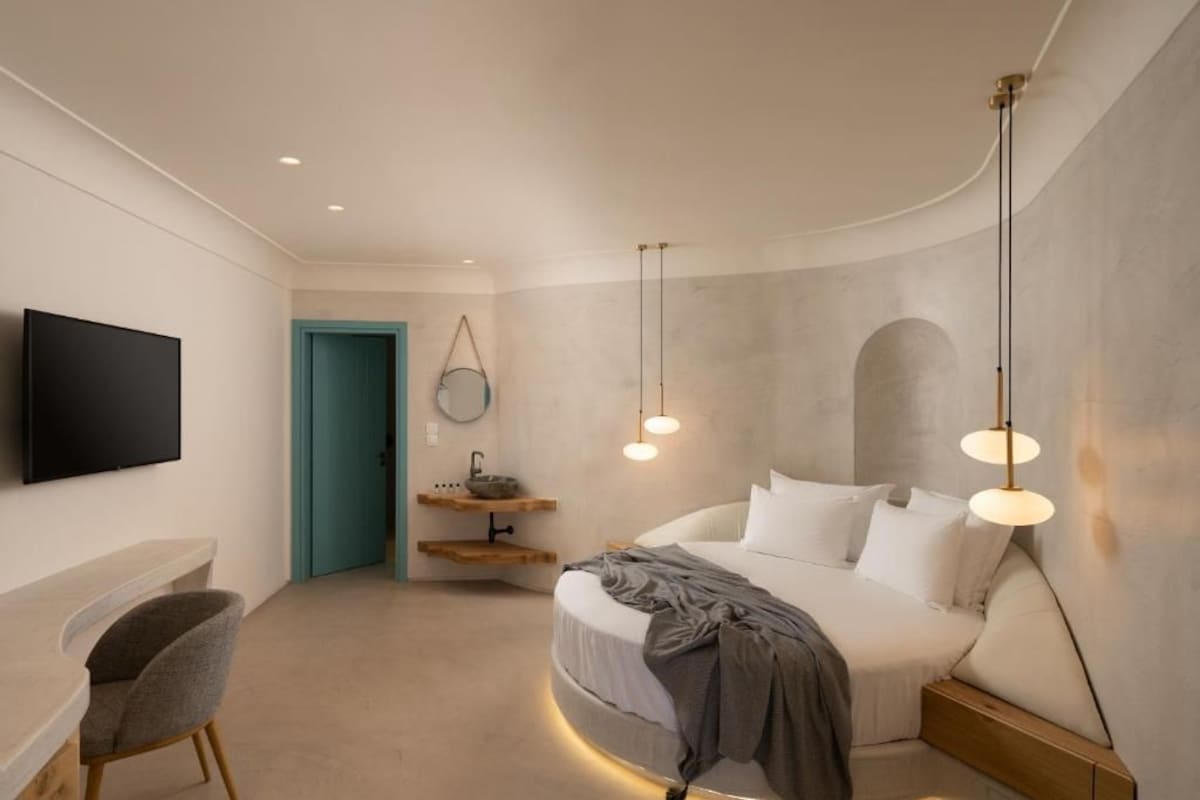 Un dormitorio moderno con una cama curvada, un televisor montado en la pared y un escritorio con una silla.
