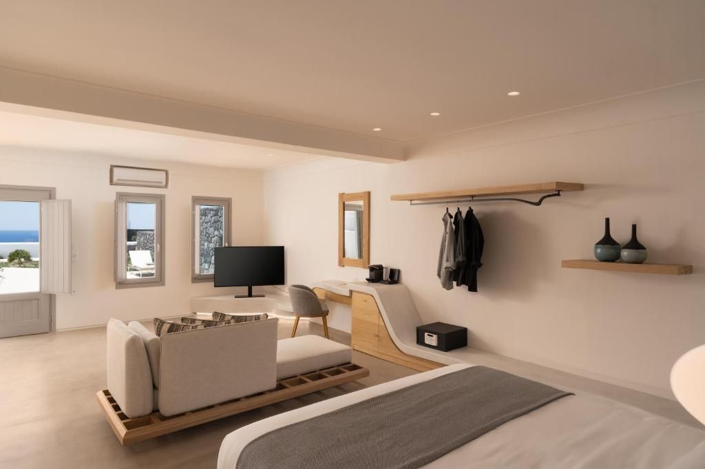 Quarto moderno com cama, escrivaninha, cadeira, televisão e vista para o mar.