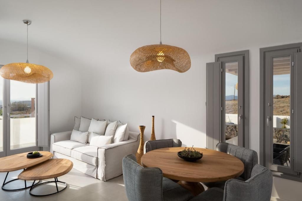 A modern living room with a white sofa, grey armchairs, a round wooden coffee table, and a hanging woven light fixture.