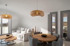 Un salon moderne avec un canapé blanc, des fauteuils gris, une table basse ronde en bois et un luminaire suspendu en fibres tressées.
